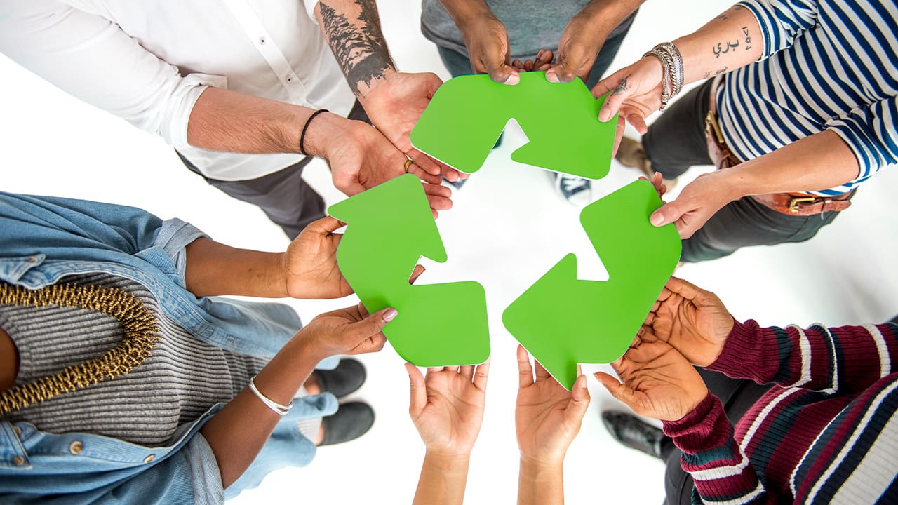 6 pessoas formando um círculo e segurando o símbolo da reciclagem no centro